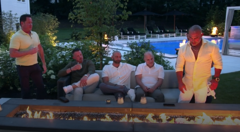 Joe Gorga throwing card into the fire. RHONJ husbands look disappointed.